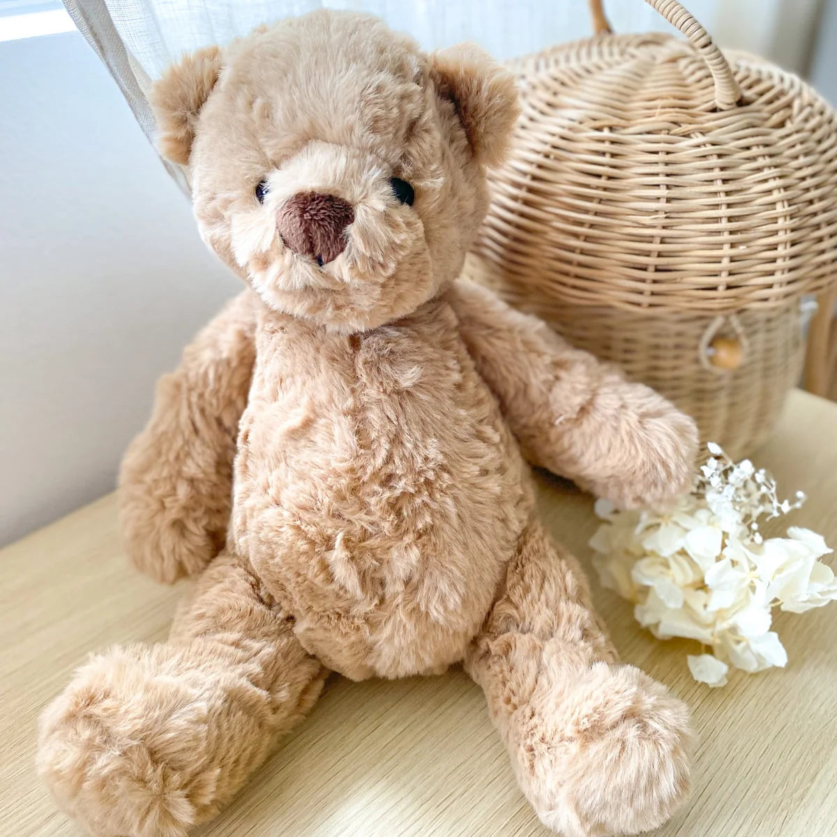 Plush teddy bear on a light surface with a wicker basket and flowers in the background